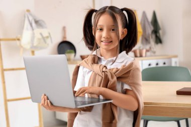 Küçük Asyalı kız mutfakta dizüstü bilgisayar kullanıyor.
