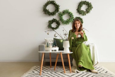 Oturma odasındaki ağaç dallarında Noel topları olan genç bir kadın.