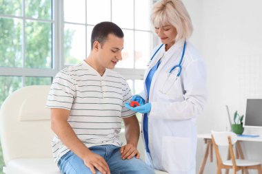 Kadın endokrinolog klinikteki kanepede tiroit bezi modelini erkeğe gösteriyor.