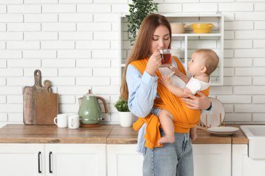 Genç anne evde küçük bebekle çay içiyor.