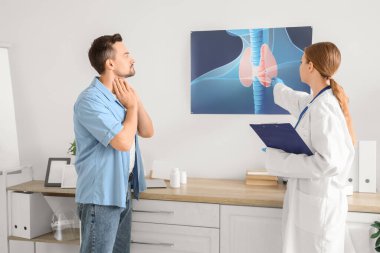 Kadın endokrinolog tiroit bezinin resmini klinikteki hastaya gösteriyor.