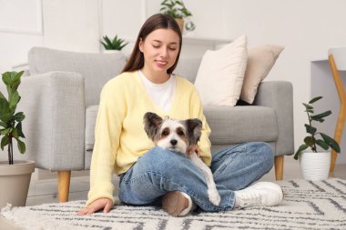 Evde halıda oturan bisikletli teriyer köpeği olan genç bir kadın.