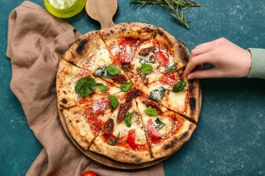 Lezzetli pizzanın üzerine fesleğen yaprağı koyan kadının eli mavi arka planda.