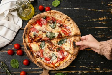 Kadın eli, siyah ahşap arka planda lezzetli bir pizza dilimi alıyor. Üst görünüm