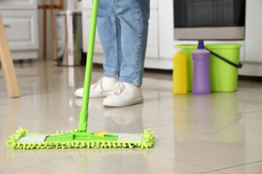 Mutfakta yerleri paspaslayan genç bir kadın.