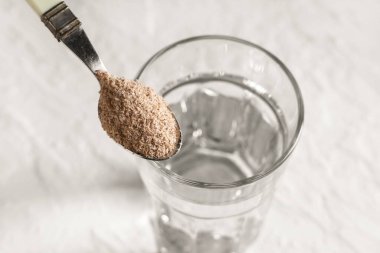 Beyaz arka planda psyllium kabuklu bir bardak su ve kaşık, yakın plan.