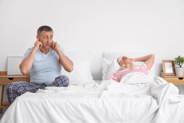 Karısının yatak odasında horlaması yüzünden sinirli, olgun bir adam kulaklarını kapatıyor.