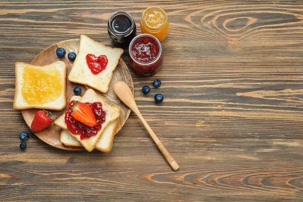 Lezzetli tost tabağı, farklı reçel kavanozları ve kahverengi ahşap arka planda böğürtlen.