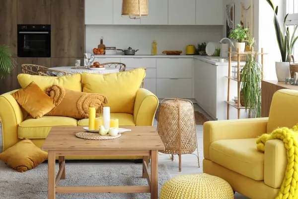 Açık uzay mutfağının içinde sarı kanepe, koltuk ve ahşap sehpa var.