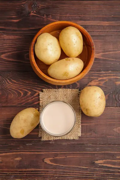 Bir bardak lezzetli patates sütü ve ahşap arka planda taze sebzeler.