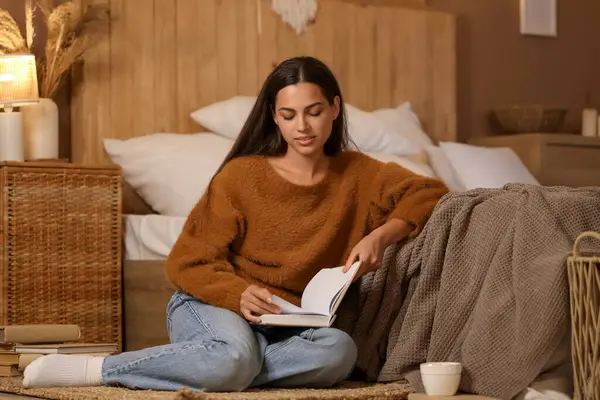 Güzel genç bir kadın akşam evde yerde kitap okuyor.