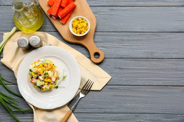 Yengeç sopalı bir tabak salata, gri ahşap arka planda mısır ve salatalık