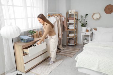 Yatak odasındaki çekmecelerden süveter çıkaran genç bir kadın.