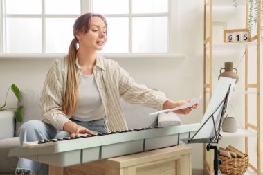 Not kâğıtlarıyla evde sentezleyici çalan genç bir kadın.