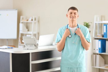 Klinikteki resepsiyon masasının yanında steteskobu olan bir erkek stajyer.