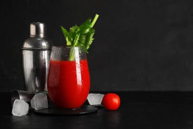 Bir bardak Bloody Mary, kereviz, buz küpleri, titretici, ölçü kabı ve domatesli siyah grunge arkaplan