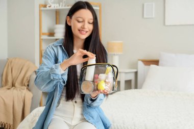 Kozmetik çantası ve makyaj malzemeleri olan genç kız yatak odasında.