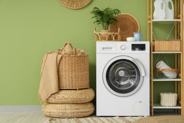 Çamaşır odasındaki yeşil duvarın yanında raflar, sepet ve deterjanlar olan modern çamaşır makinesi.
