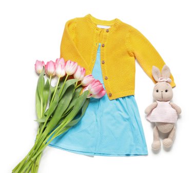 Tavşan oyuncağı ve beyaz arka planda laleleri olan küçük bir kız bahar kıyafeti.