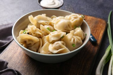 Koyu arkaplanda yeşil soğanlı ve ekşi kremalı bir kase lezzetli haşlanmış hamur köftesi.