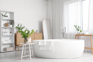 Küveti, raf ünitesi, aynası, klozeti ve masaların üzerindeki vazolarda çiçek açan yeşil dalları olan şık bir banyo.