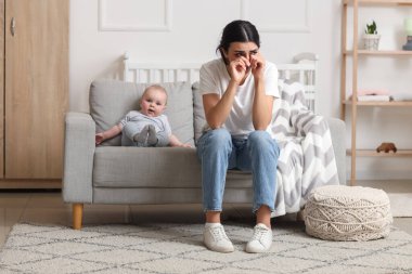 Doğum sonrası depresyondan muzdarip ağlayan anne bebeğiyle birlikte evdeki kanepede yatıyor.