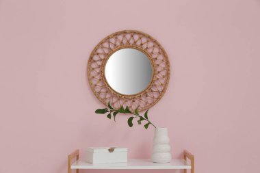Raflarda yeşil dalı olan vazo ve pembe duvarda yuvarlak ayna, yakın plan.