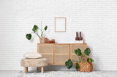 Modern oturma odasının içinde çekmeceler, puf ve Monstera bitkileri var.