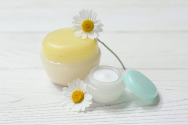 Kavanozlar dolusu papatya çayı ve beyaz ahşap arka planda çiçekler.