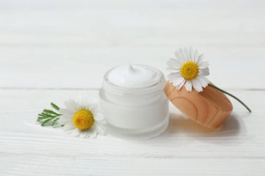Bir kavanoz papatya çayı kozmetik kremi ve beyaz ahşap arka planda çiçekler.