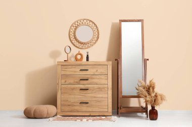 Döşeme aynası, çekmece sandığı ve odanın içindeki bej duvarın yanındaki puf.