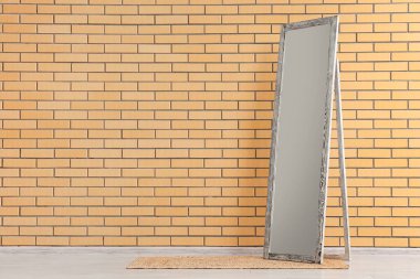 Bej tuğlalı duvarın yanında büyük bir ayna ve halı var.