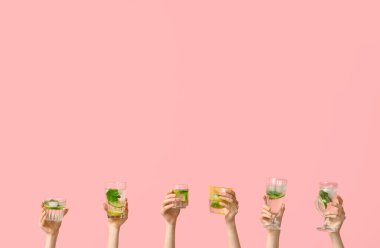 Pembe arka planda farklı bardaklarda taze mojito tutan kadın eller.