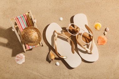 Arka plan olarak şık parmak arası terlikleri, güneş gözlükleri, dekoratif şapkası ve güverte koltuğu olan kompozisyon, yakın plan.