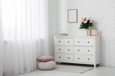 Pouf, çekmece ve vazo. Odanın içinde güzel şakayık çiçekleri var.