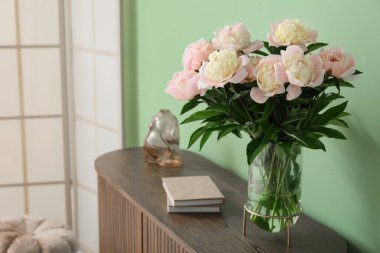 Odadaki yeşil duvarın yanındaki çekmecelerin üzerinde güzel şakayık çiçekleri olan kitaplar ve vazolar.