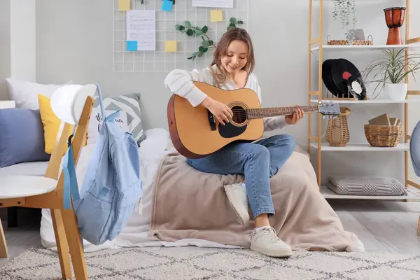 Genç bir kadın yatak odasında gitar çalıyor.