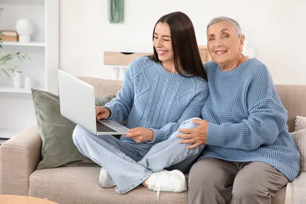 Bilgisayarlı ve büyükannesi evdeki kanepede oturan mutlu genç bir kadın.