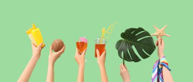 Kokteyl, hindistan cevizi, güneş kremi, deniz yıldızı ve yeşil arka planda canavar yaprağı olan kadın elleri. Seyahat kavramı