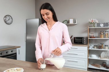 Güzel bir kadın mutfakta bardağa süt dolduruyor.