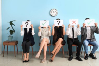 Genç adaylar odada farklı notlarla kağıt çarşaf tutuyorlar.