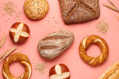 Different types of bread and wheat ears on pink background