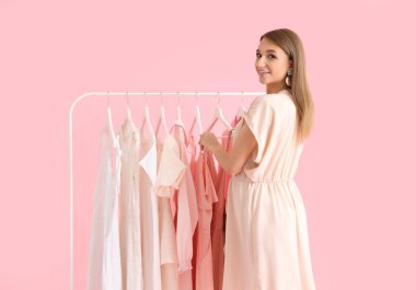 Güzel, mutlu, genç bir kadın ve pembe arka planda farklı stil kıyafetleri olan göğüsler.