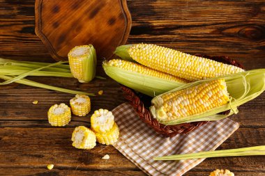Tahta arka planda taze mısır koçanları olan sepet.