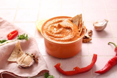 Bir kase lezzetli muhammara ve pembe fayanslı malzemeler.