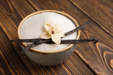 Aromatik vanilya şekeri, çiçek ve tahta arka planda sopalarla dolu bir kase.