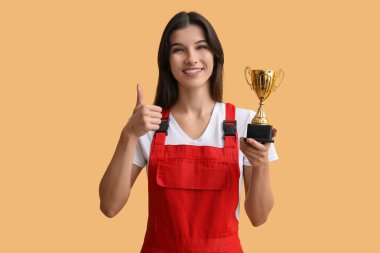 Altın bardaklı kadın işçi sarı arka planda baş parmağını gösteriyor.