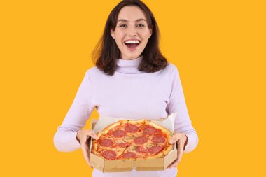Sarı arka planda lezzetli pepperonili pizzalı genç bir kadın.