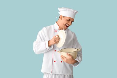 Mavi arka planda tenceresi olan yakışıklı, mutlu bir aşçı.