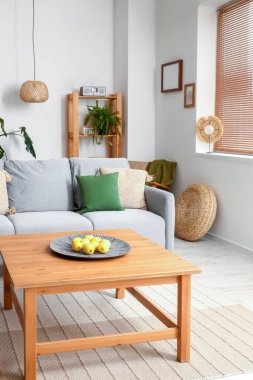 Oturma odasının iç tarafındaki ahşap sehpada limonlu rahat gri kanepe ve tabak.